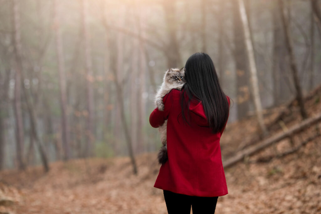Woman holding her cat over her shoulder ready to head over to Happy Tails Grooming in Franklin MA after her kitty played in the fall leaves.