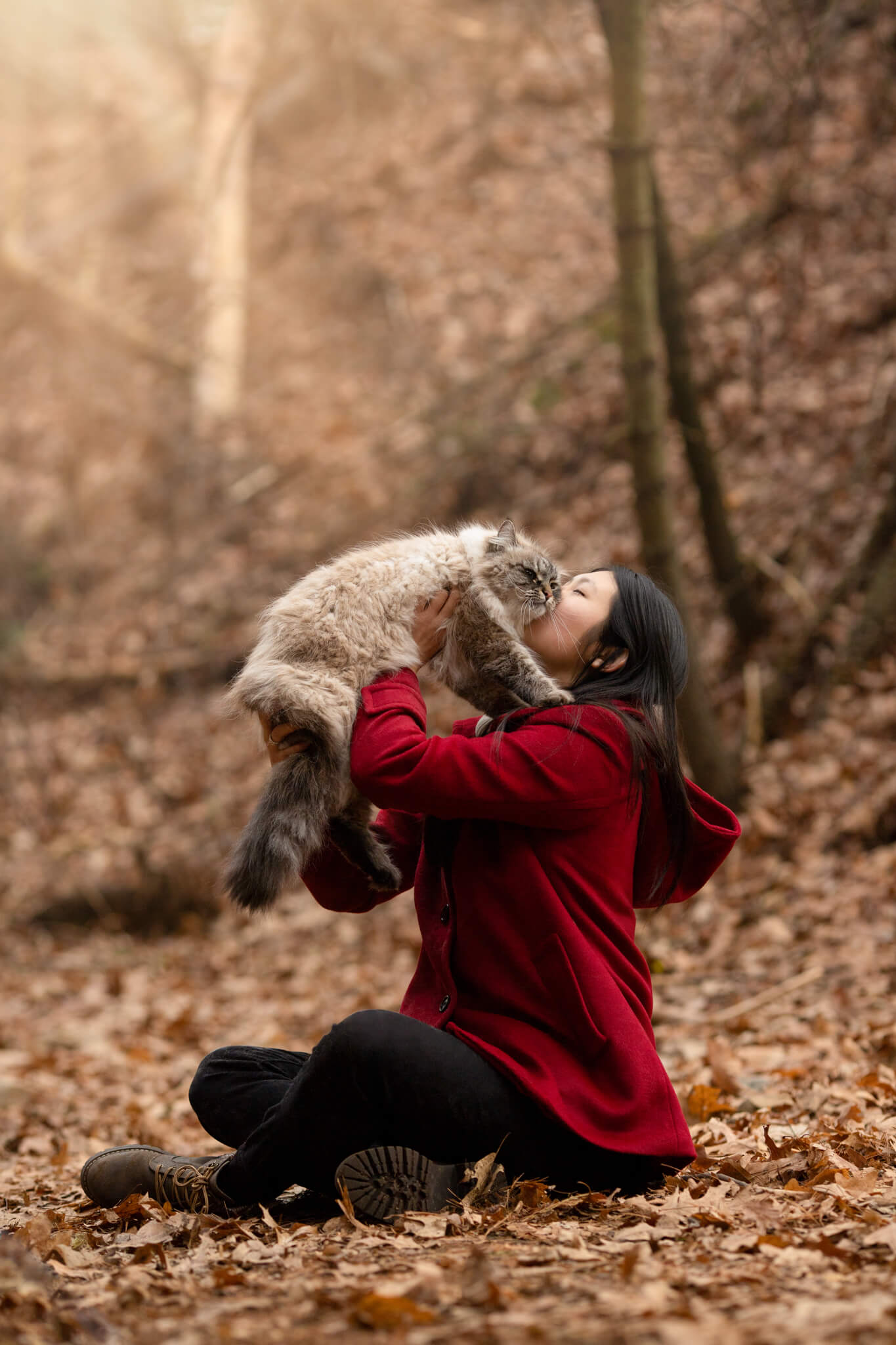 woman in red jacket sitting in the woods holding her cat up in the air Bark N Roll Reading MA