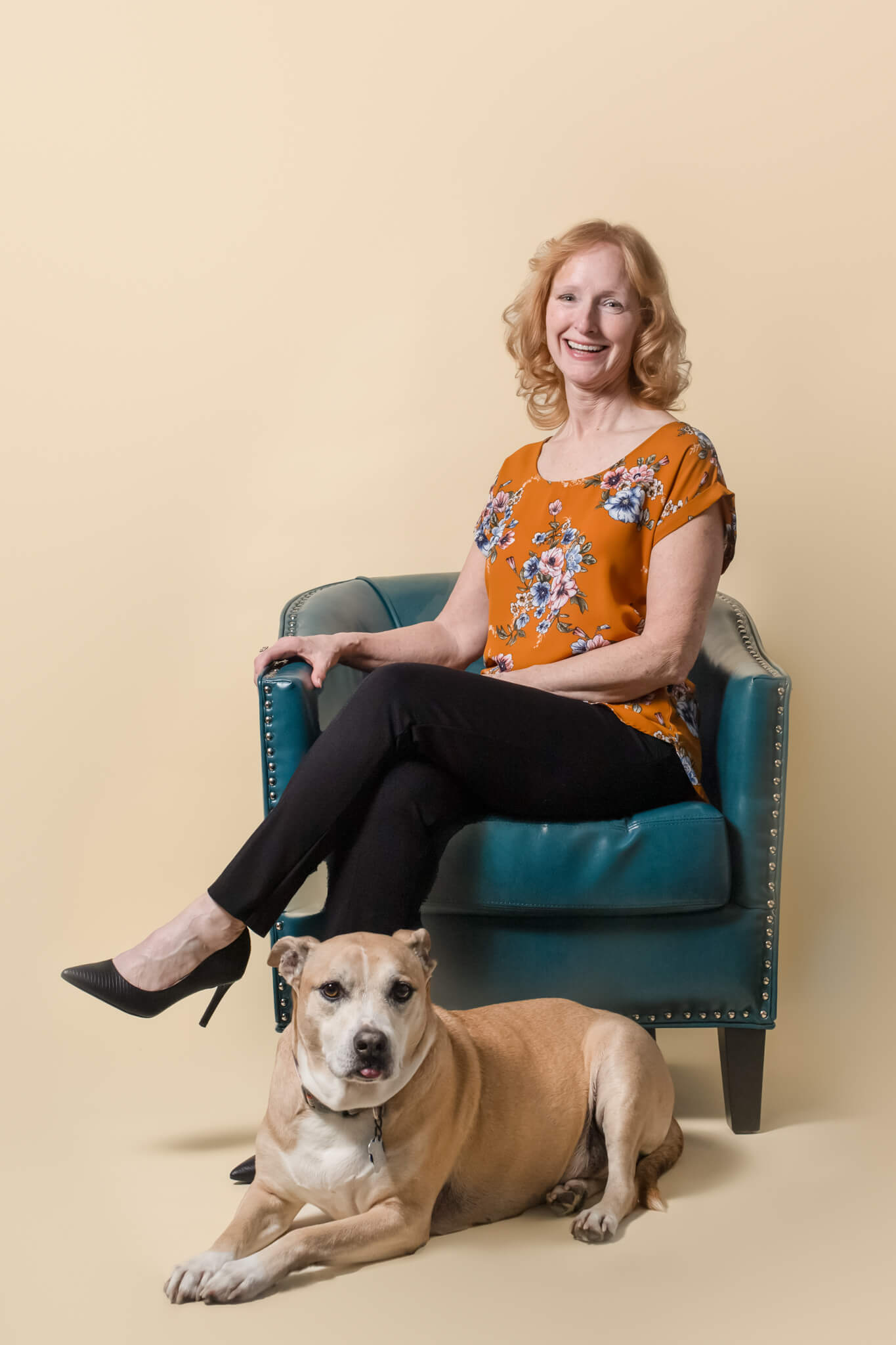 Woman sits on a blue leather chair with her brown dog laying in front of her tufts animal hospital